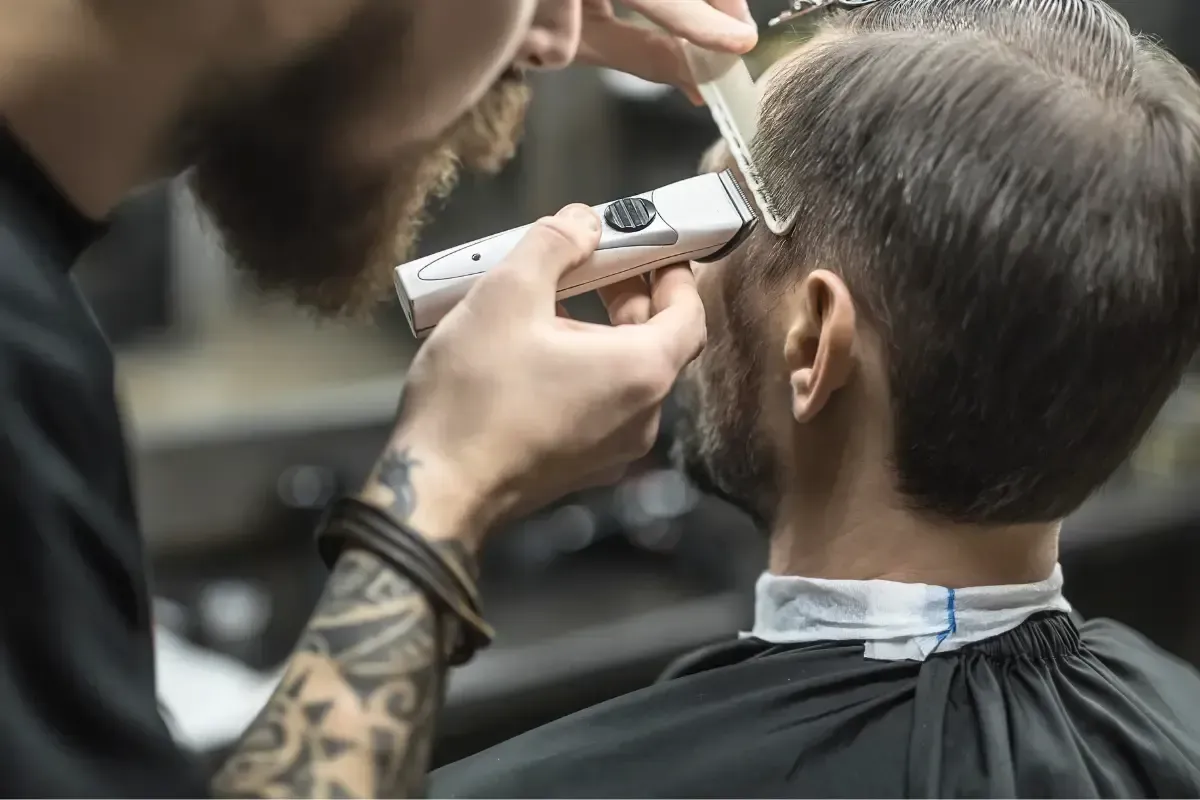 Barber trimming the side of a man’s haircut with clippers and comb