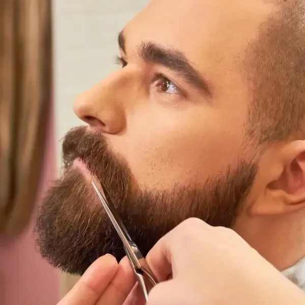 Barber trimming and shaping a full beard with scissors for a sharp finish