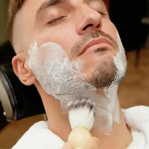 Barber applying hot lather with a brush for a traditional straight razor shave
