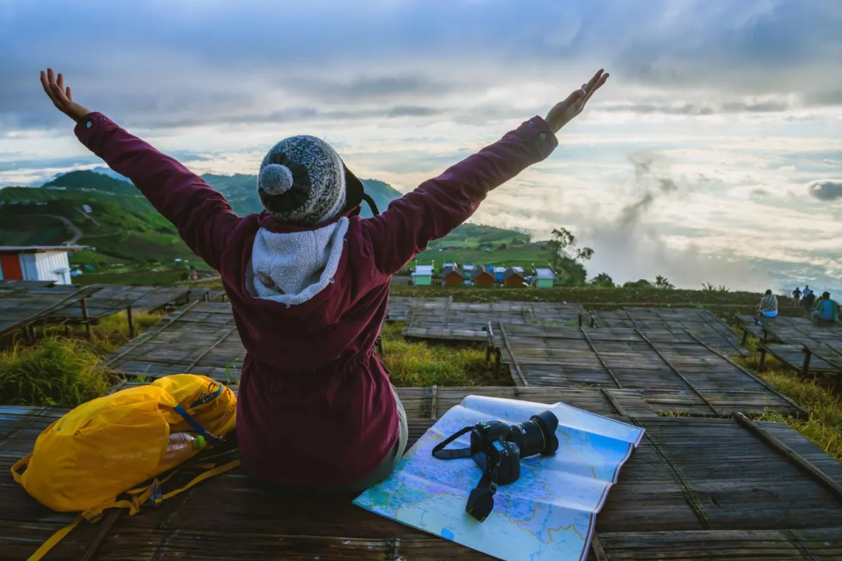 Image of a person sitting atop a hill enjoying the scenery with arms outstretched