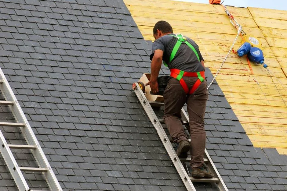 Man on a ladder working to install a steep shingle roof.