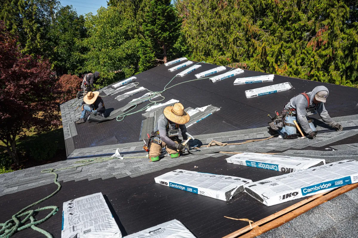 4 roofing workers on top of a roof diligently working to install a new asphalt roof.