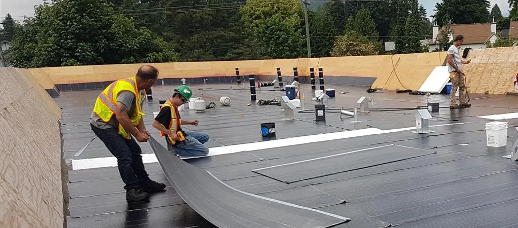 Image of roofing workers actively installing a flat roofing system atop a building.