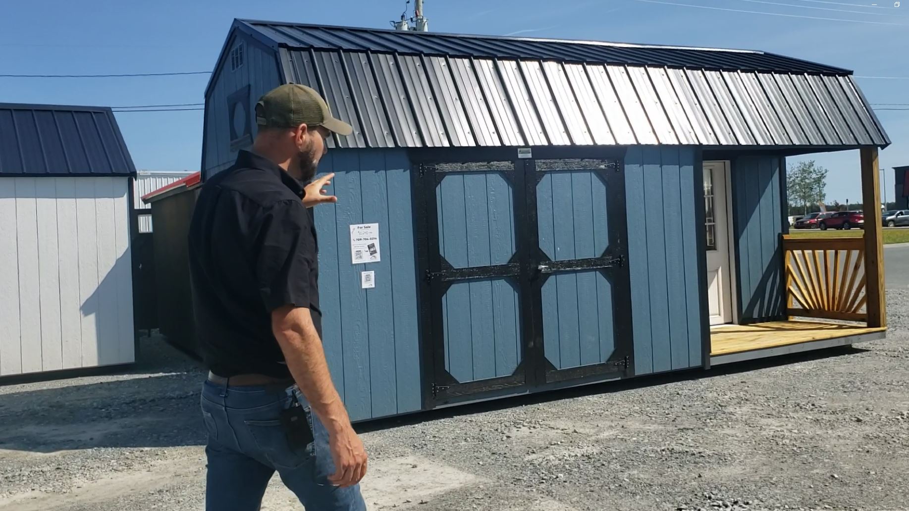 A friendly, middle-aged man and woman in casual workwear standing in front of a row of colorful sheds, holding a Digital Shed CRM sign, rural background, bright sky, authentic and approachable vibe.