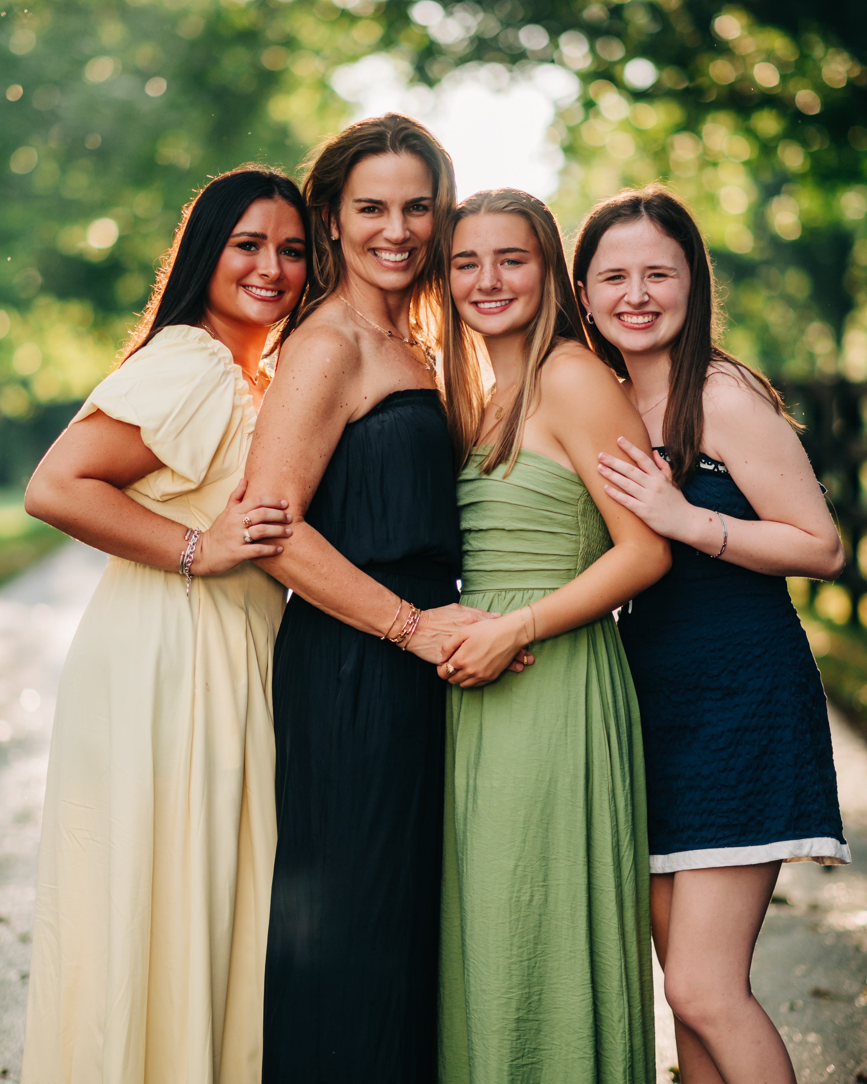 Four women stand close together outdoors, arms wrapped around one another and smiling warmly (Evidence), sharing a moment of joy, pride, and deep connection (Emotion), reflecting the strength of belonging and the relationships that shape who they are becoming together (Elevation)