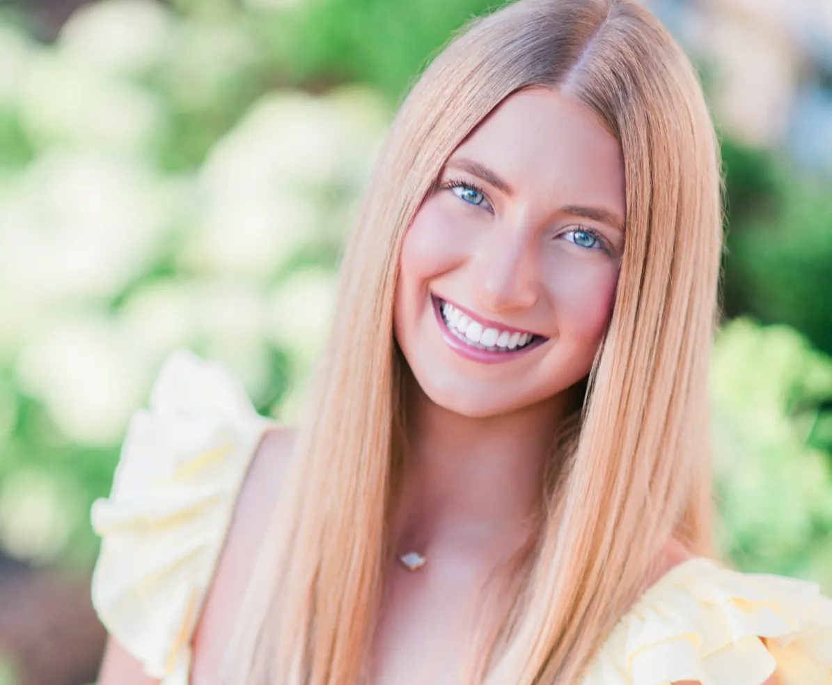 Nashville high school senior with long blonde hair and a bright, easy smile, wearing a pale yellow ruffled dress in front of soft white summer hydrangeas.