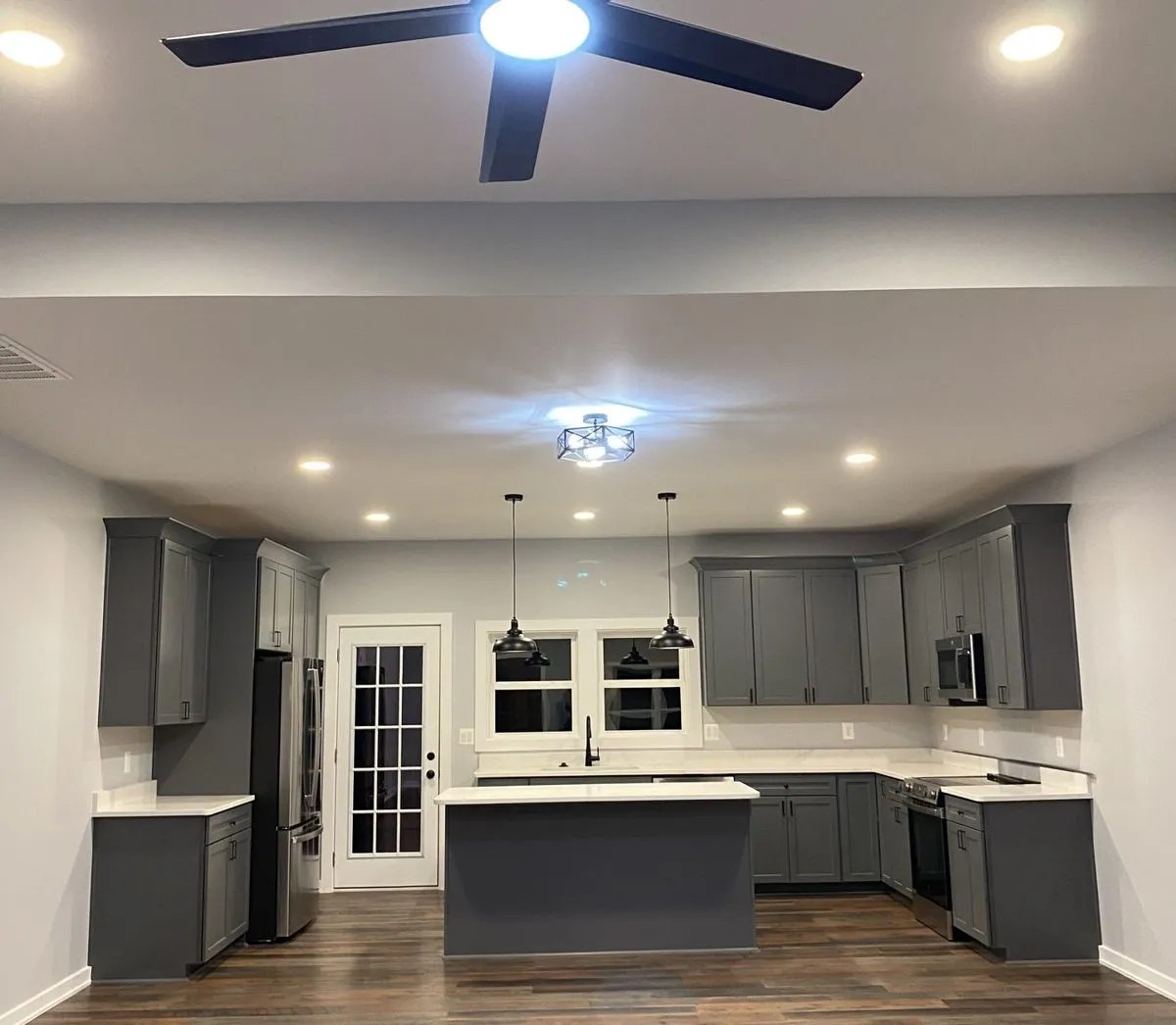 Open living room and kitchen in a new home with gray shaker cabinets, island pendants and wood-look plank flooring