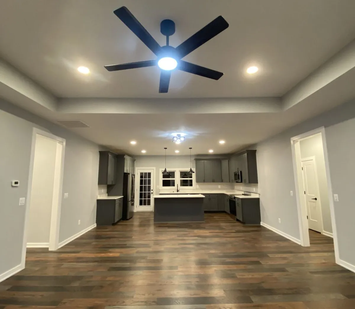 Wide view of an open-concept living room and kitchen with a tray ceiling in a new home