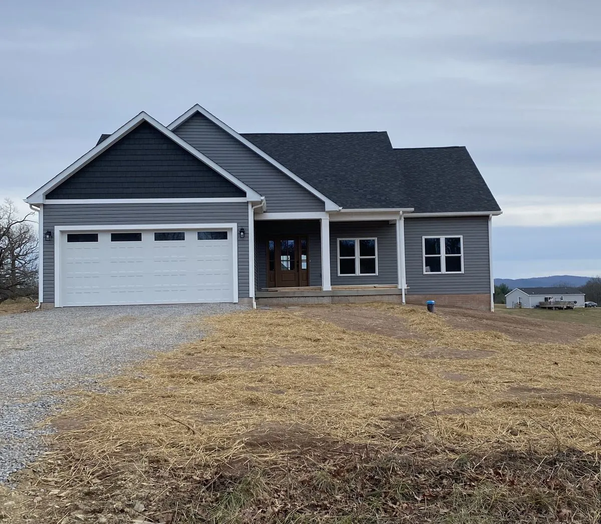 Front exterior of a newly built single-story home with gray siding, white two-car garage door and wood front door, Winchester, VA