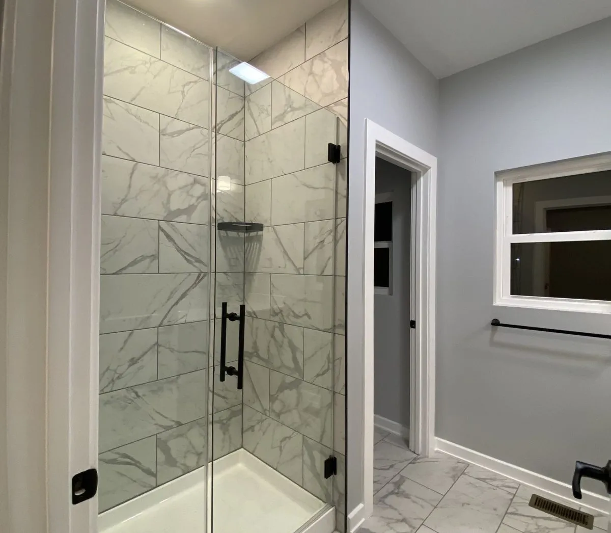 Bathroom with glass walk-in shower, marble-look tile floor and black towel bar