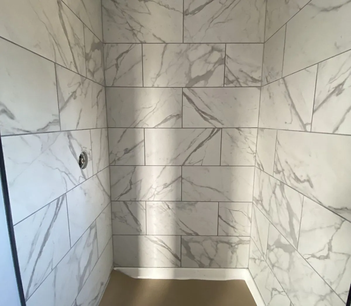 Walk-in shower under construction with large marble-look tile walls