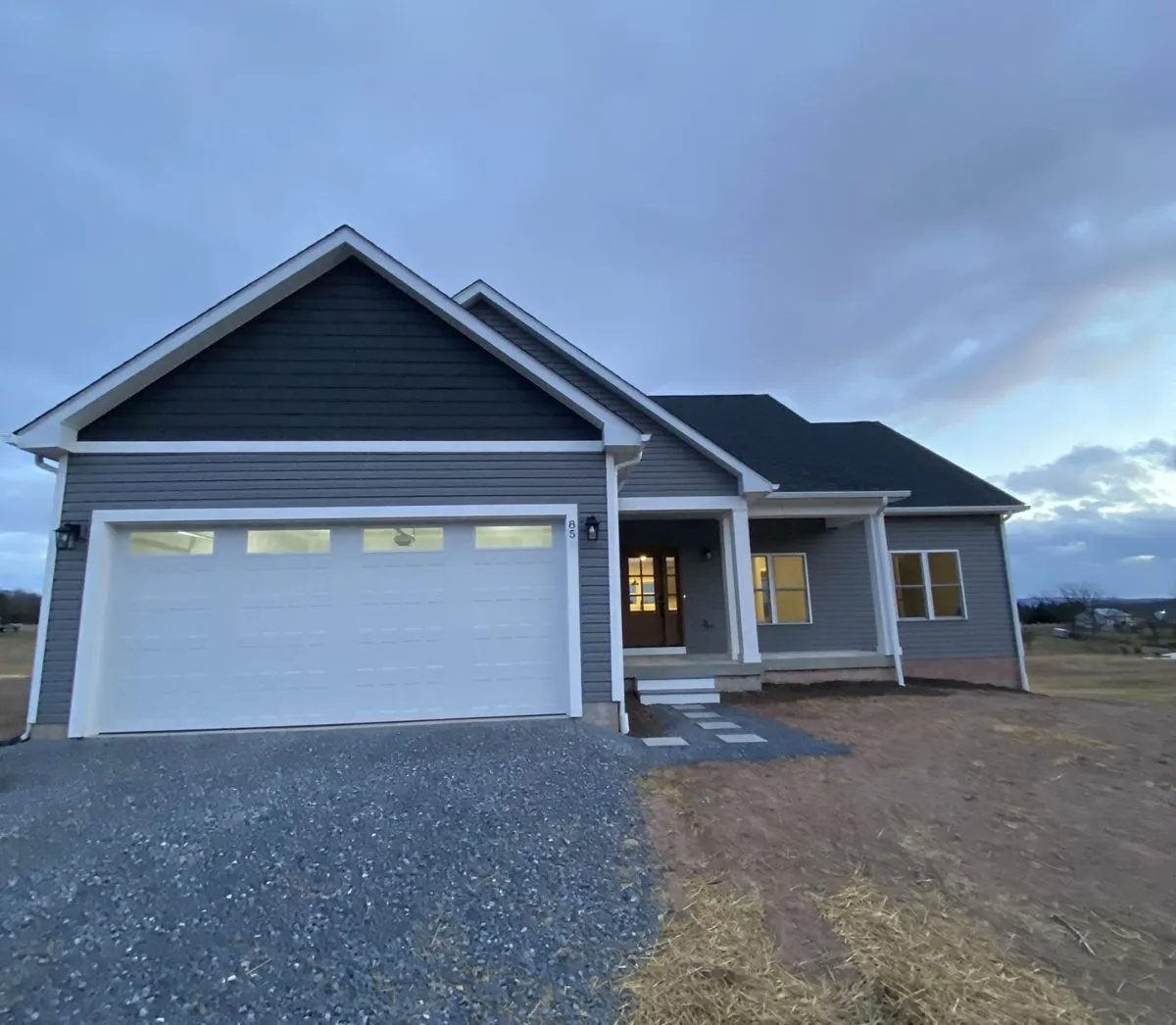 Newly built single-story home at dusk with interior lights on and a paver walkway, Winchester, VA