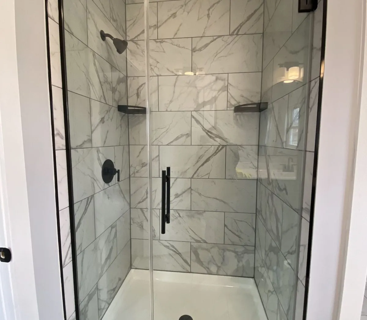 Finished walk-in shower with marble-look tile, frameless glass door and matte black fixtures