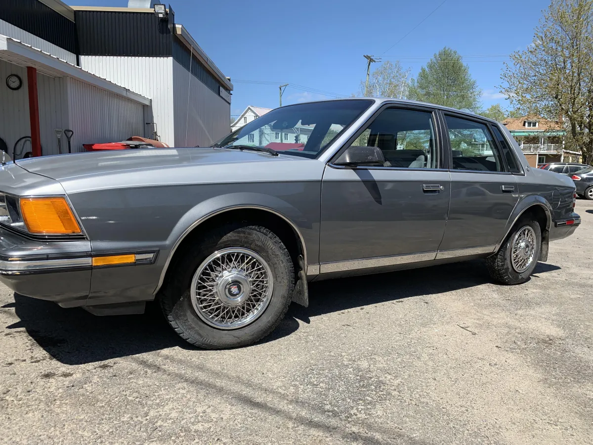 Voiture berline grise entièrement restaurée avec carrosserie réparée et peinture uniforme, stationnée devant le garage.