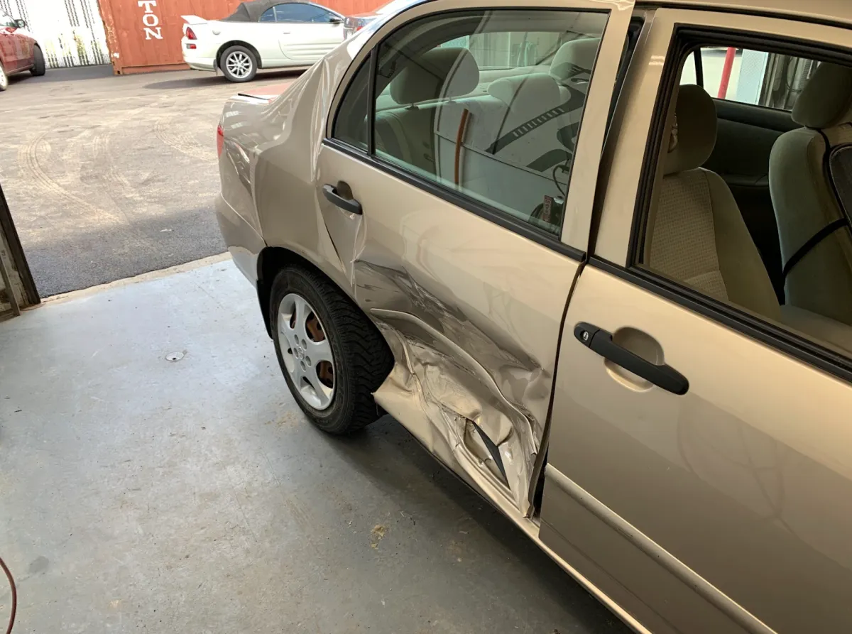 Portière arrière enfoncée sur une voiture beige, dommage visible causé par impact, en attente de réparation.