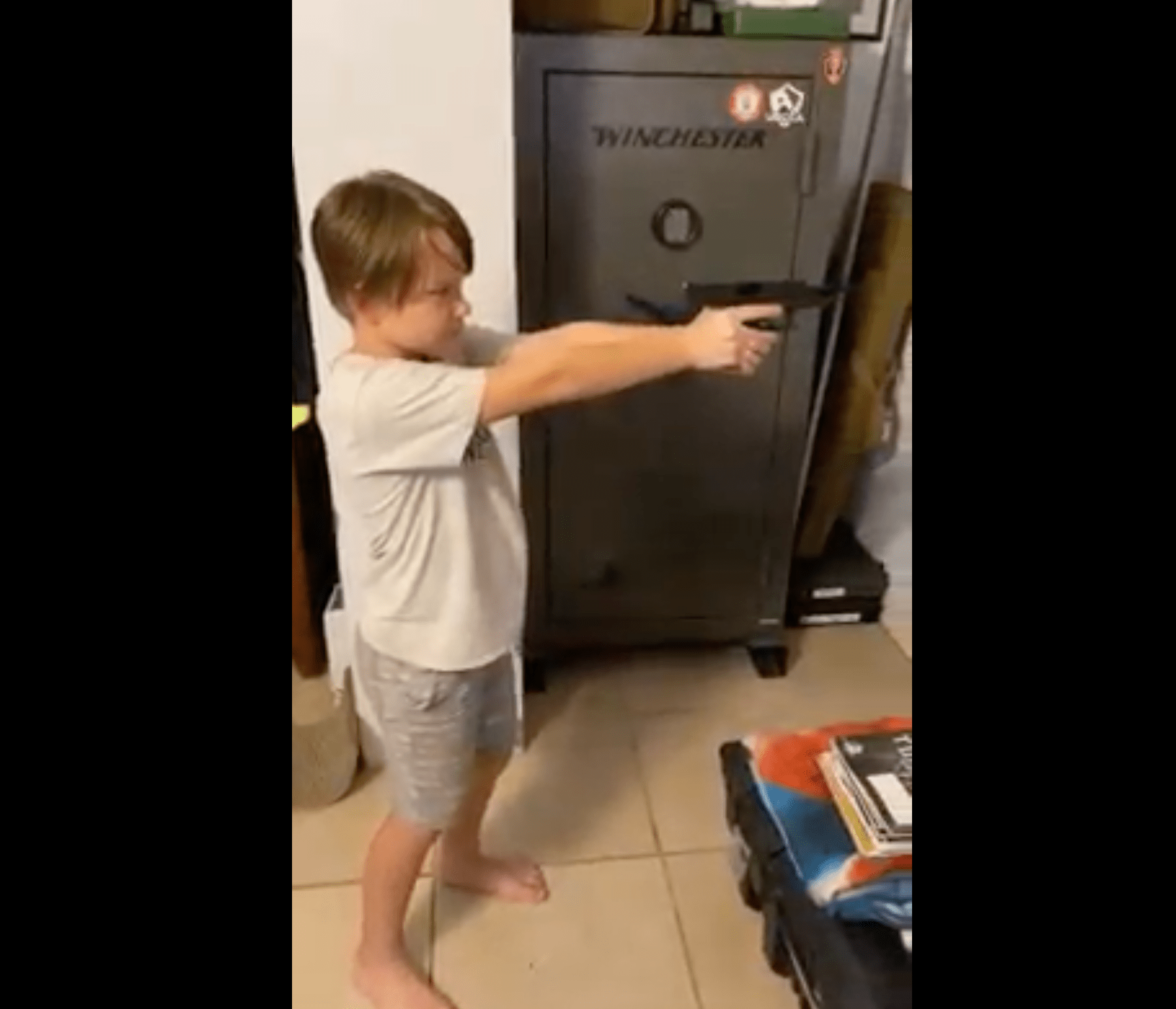 Boy holding gun practicing grip and stance indoors in front of safe