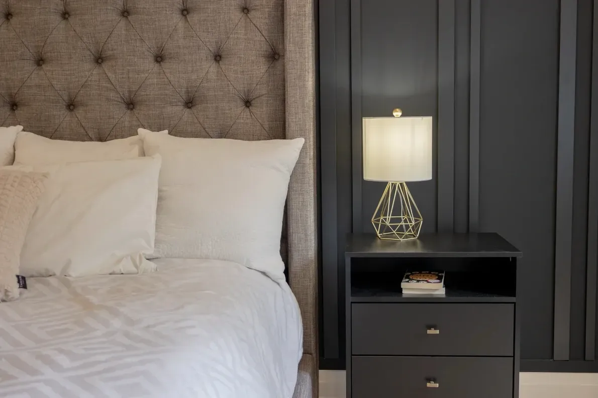 Modern renovated bedroom with dark accent wall, upholstered bed, wood nightstands and contemporary lighting
