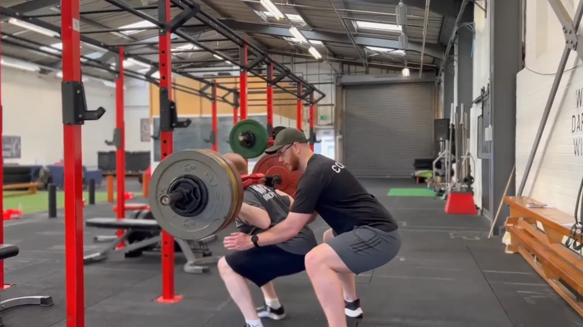 Man being supported and coached weight lifting in a fitness class at Body Transform Fitness Norwich