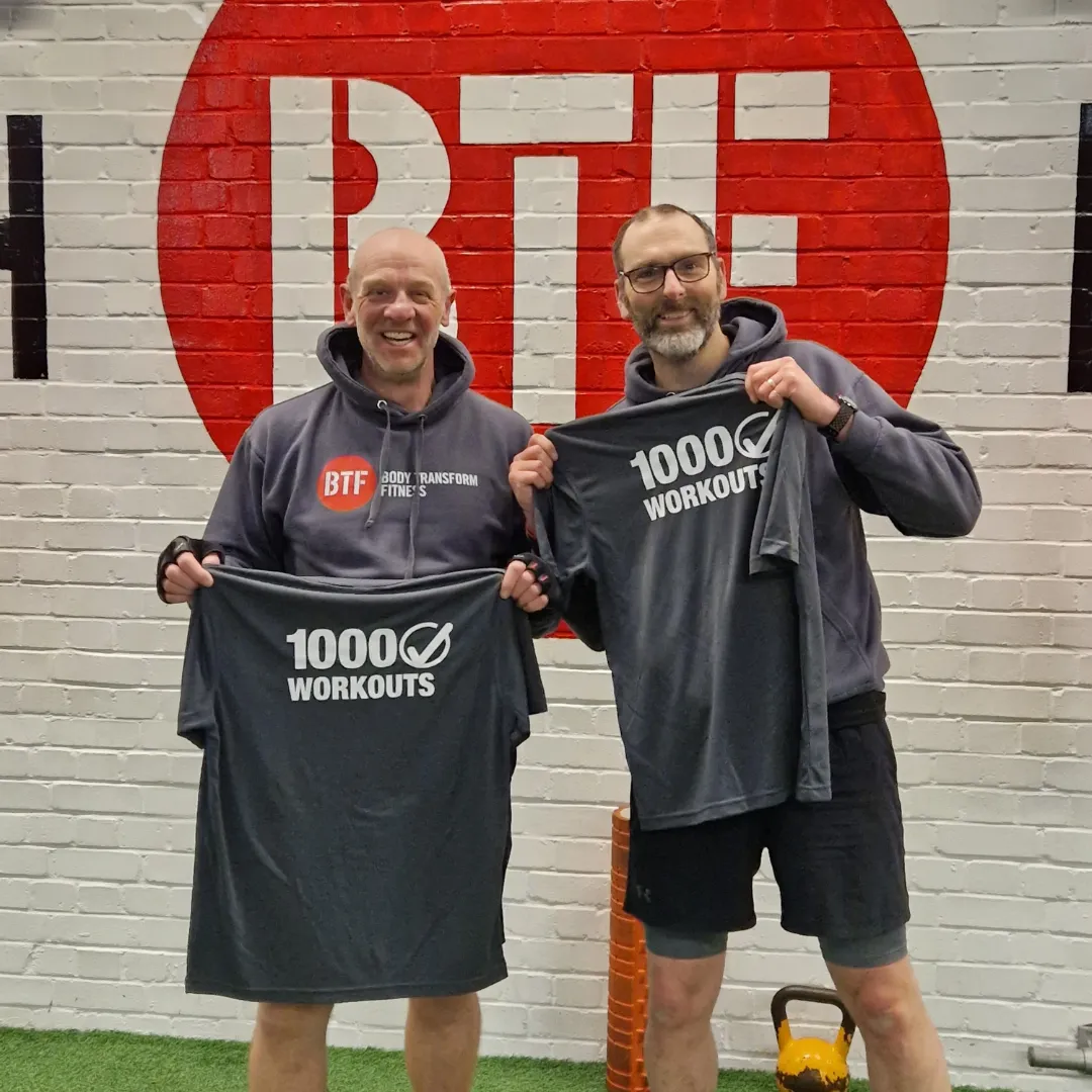 2 friends holding a t-shirt with 1000 workouts at Body Transform Fitness Norwich