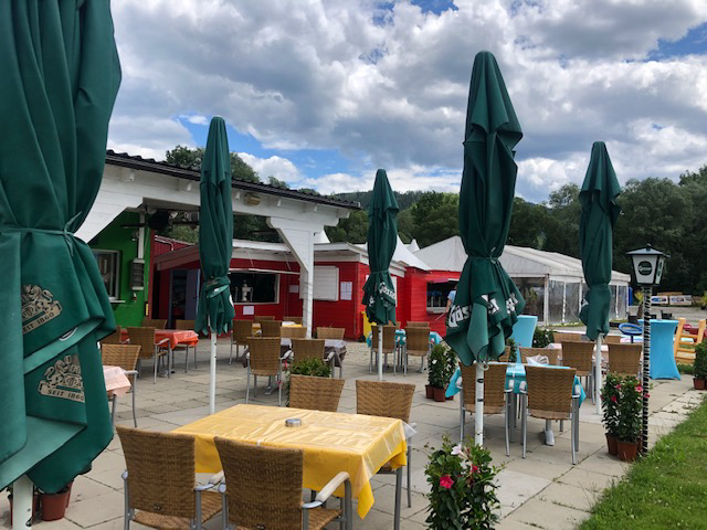 Außenbereich mit Sitzplätzen bei Flasch City highway stop near steiermark mit Tischen, Stühlen, Sonnenschirmen und Restaurantbereich