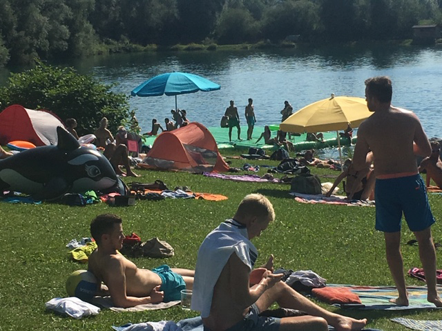Besucher entspannen und sonnenbaden am Badesee bei Flasch City near Kindberg waehrend andere im Wasser baden und den Sommertag geniessen