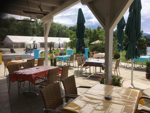 Ueberdachter Aussenbereich der Restaurant-Cafe Terrasse am Badesee bei Flasch City near Zeltweg mit Sitzplaetzen und Blick Richtung Eventzelte