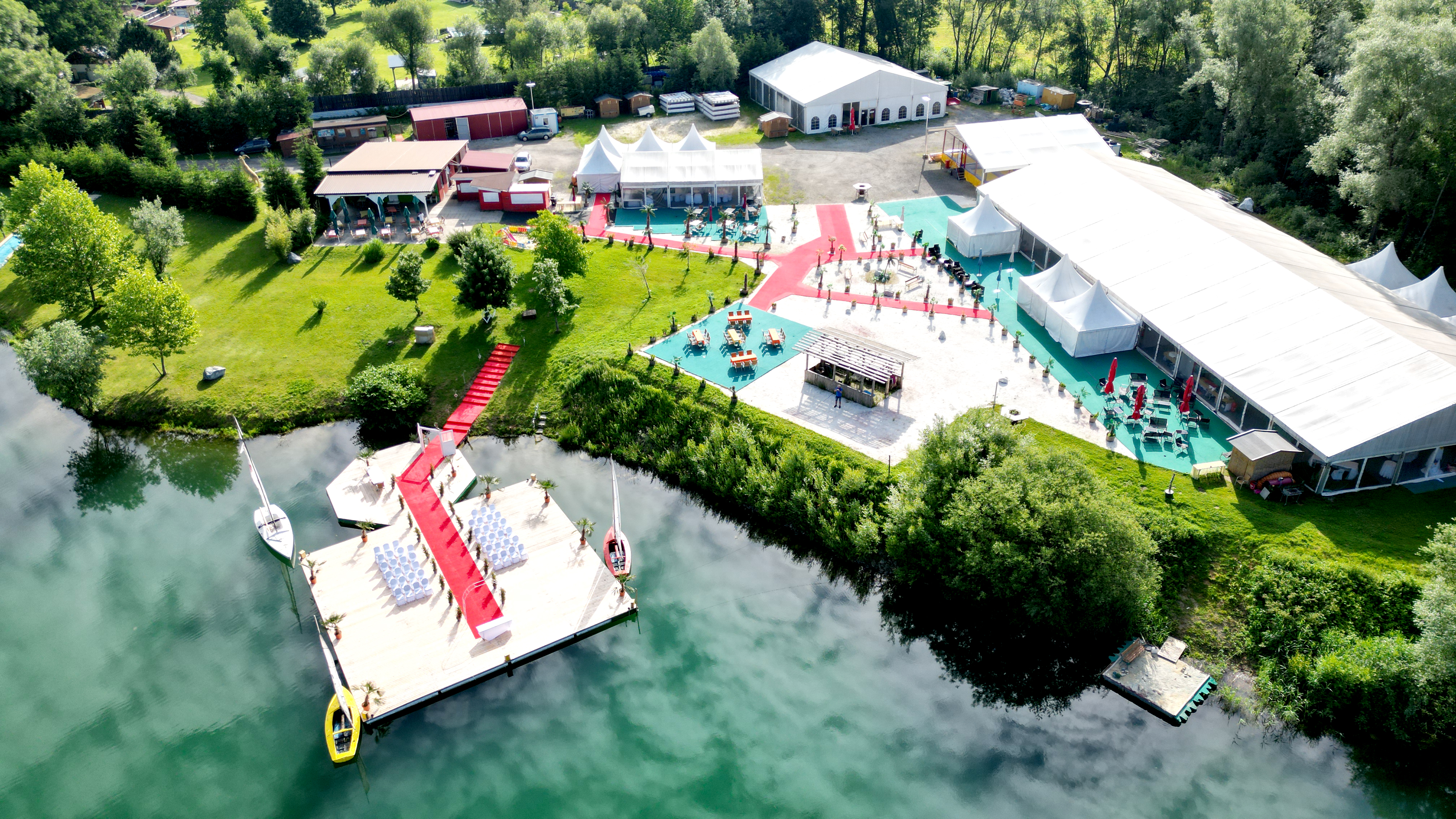 Luftaufnahme eines Stegs am Badesee bei Flasch City near Gloggnitz mit Eventaufbau und rotem Teppich, verbunden mit dem Hauptgelaende