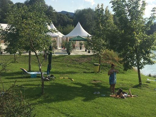 Besucher entspannen auf der Liegewiese am Badesee bei Flasch City near Wiener Neustadt mit Baeumen, Freiflaechen und nahegelegenen Eventzelten