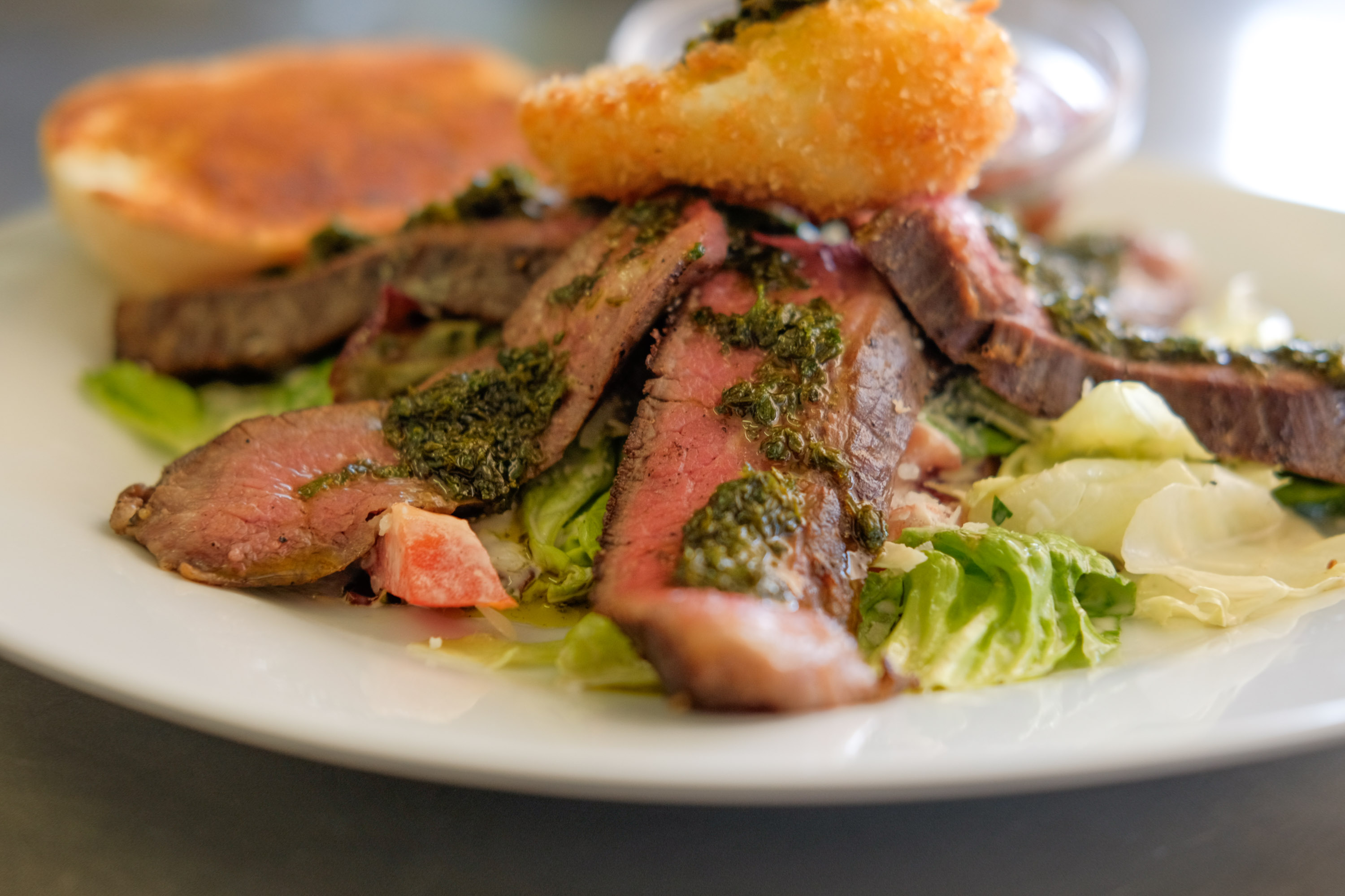 Nahaufnahme von geschnittenem medium-rare Steak auf frischem Salat mit Kräutersauce und Brot im Flasch City steak restaurant-cafe near obersteiermark