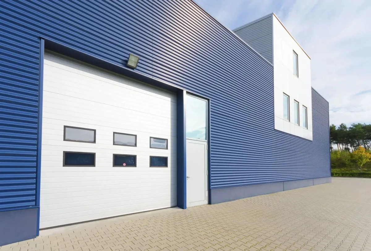Modern blue industrial warehouse exterior with a large white garage door.