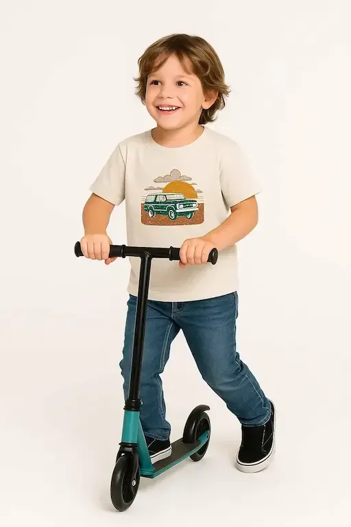 Smiling child in blue jeans and a vintage van t-shirt rides a teal scooter, showcasing original, eco-friendly cotton toddler clothing.