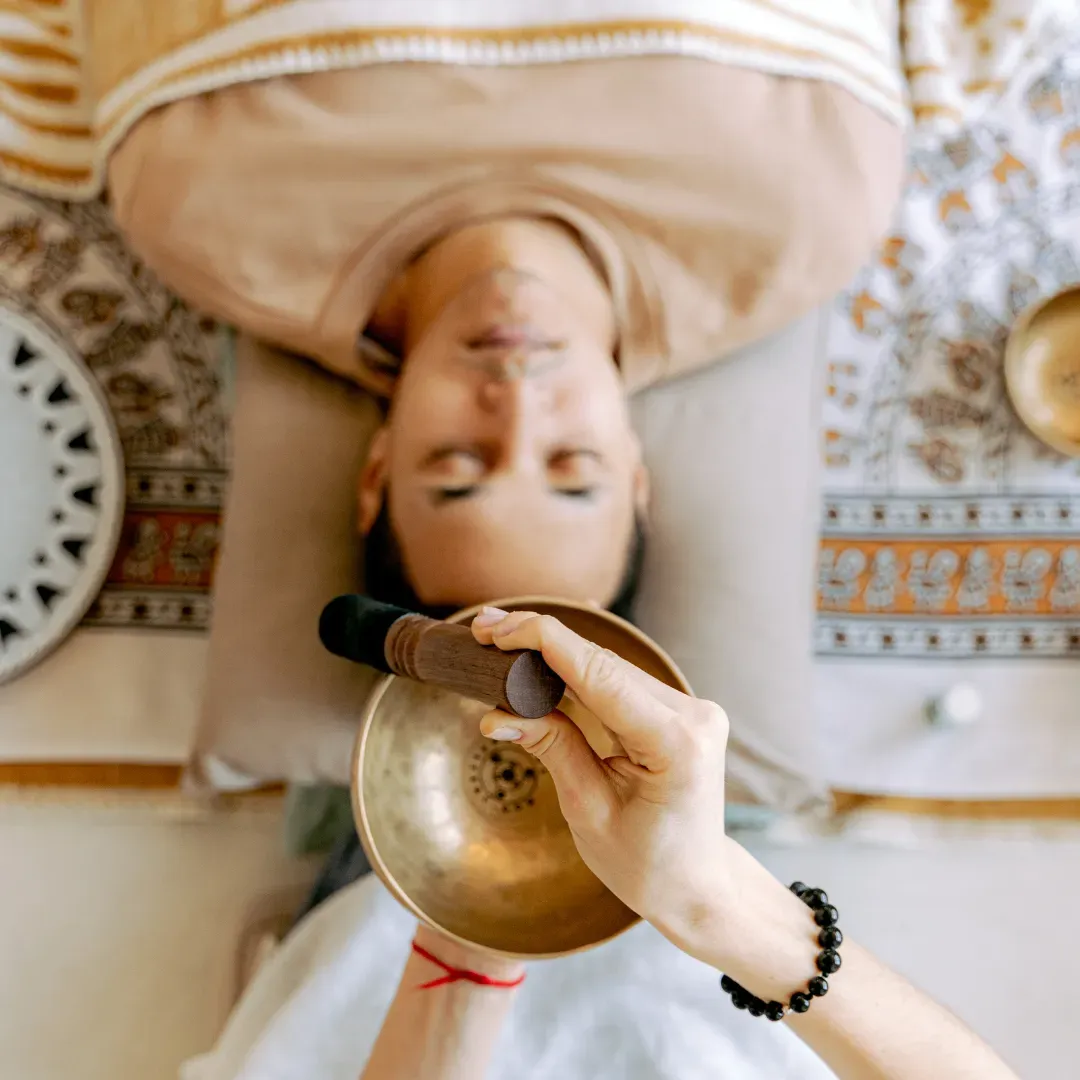 Sound healer using a singing bowl over a client lying comfortably during a calming sound healing session.