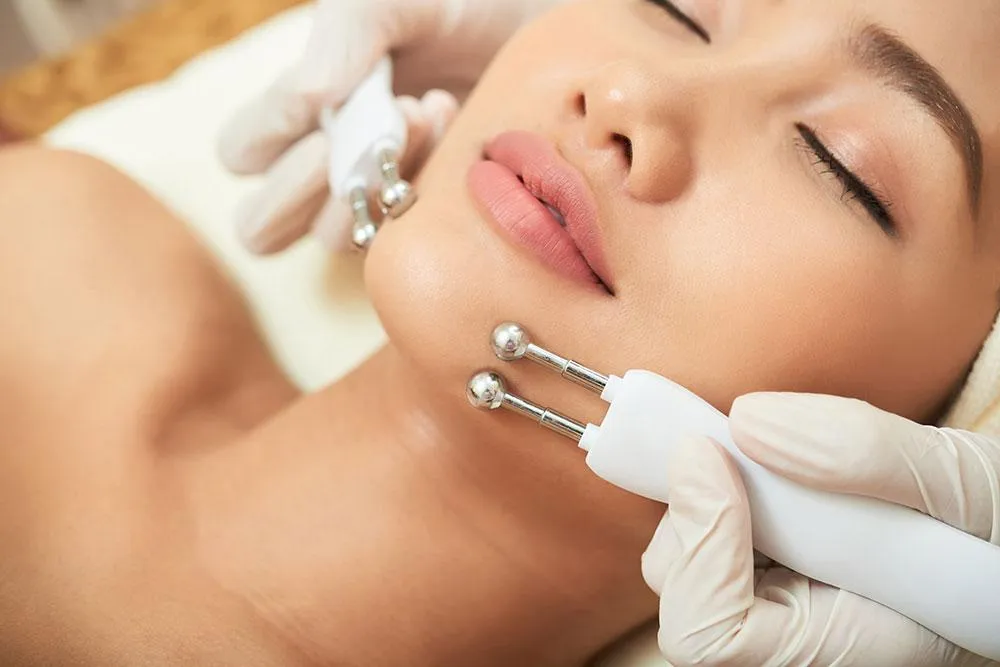 Esthetician performing a microcurrent facial treatment on a woman’s face to lift and tone facial muscles.