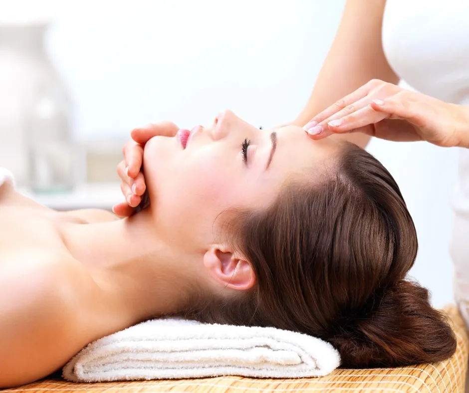 Therapist performing a cranial and neck massage on a woman lying on a spa table for tension relief.