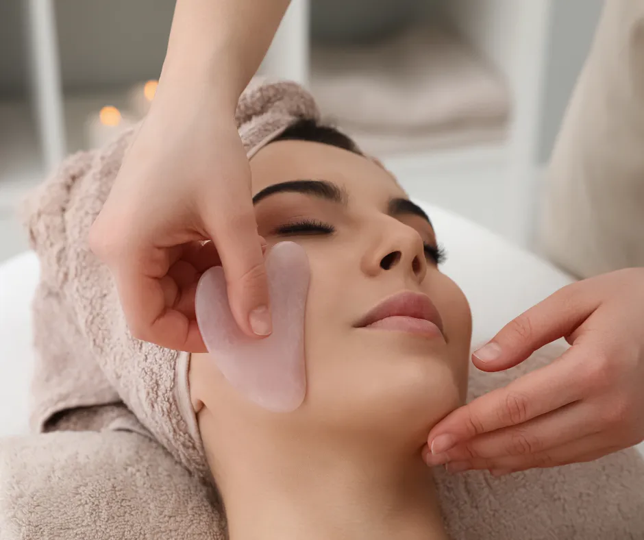 Esthetician performing a sculpting and lymphatic facial using a gua sha tool on a client’s face.