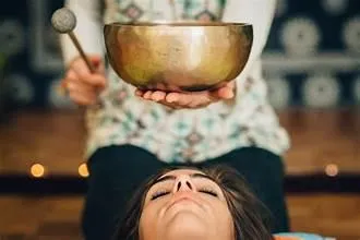 Sound healing practitioner holding a Tibetan singing bowl above a client’s head during a vibrational therapy session.