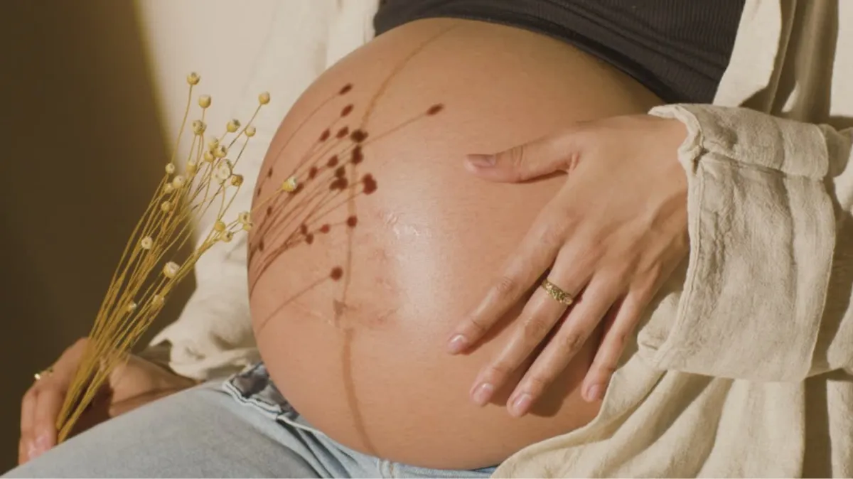 Pregnant woman holding flowers and bare, round belly
