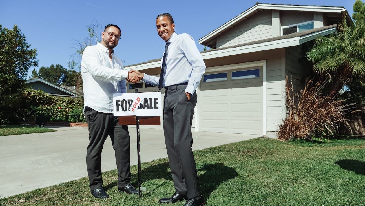 Two people shaking hands in front of a house with For Sale sign - Virginia real estate without a realtor