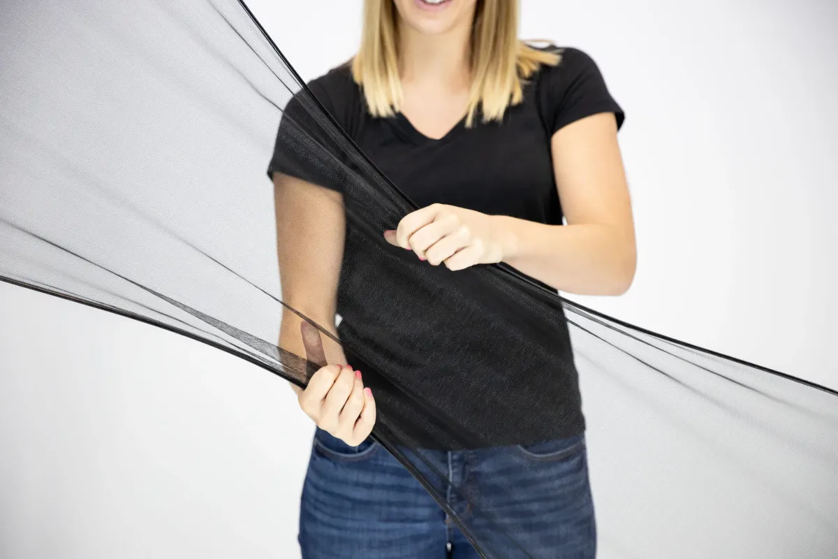 A candid shot of a homeowner installing a flexible window screen with one hand, the mesh nearly invisible against a bright, sunlit background. The image captures the ease of use and modern design of the FlexScreen technology.