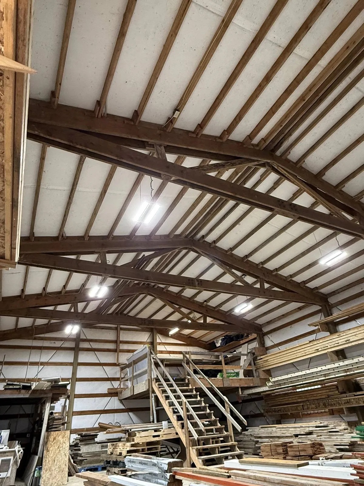 Overhead lighting installed on timber trusses in a pole building workshop