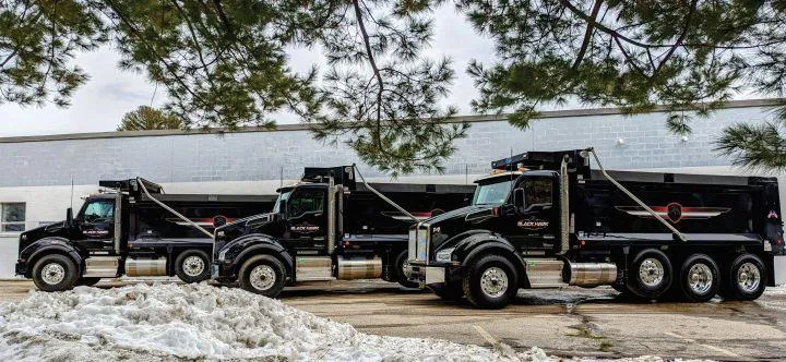 Black Hawk Paving heavy-duty trucks parked in a row, prepared for commercial paving work.