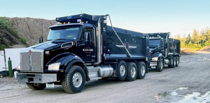 Black Hawk Paving fleet of black dump trucks lined up on a dirt road, ready for asphalt paving projects.