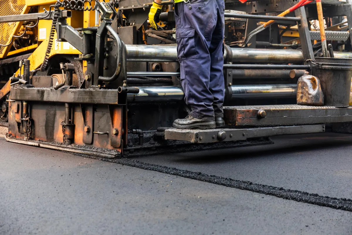 Construction worker operating heavy machinery for commercial paving on a road.