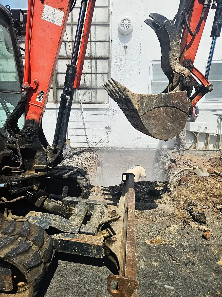 Excavator digging a trench at a construction site next to a building during underground utility work.