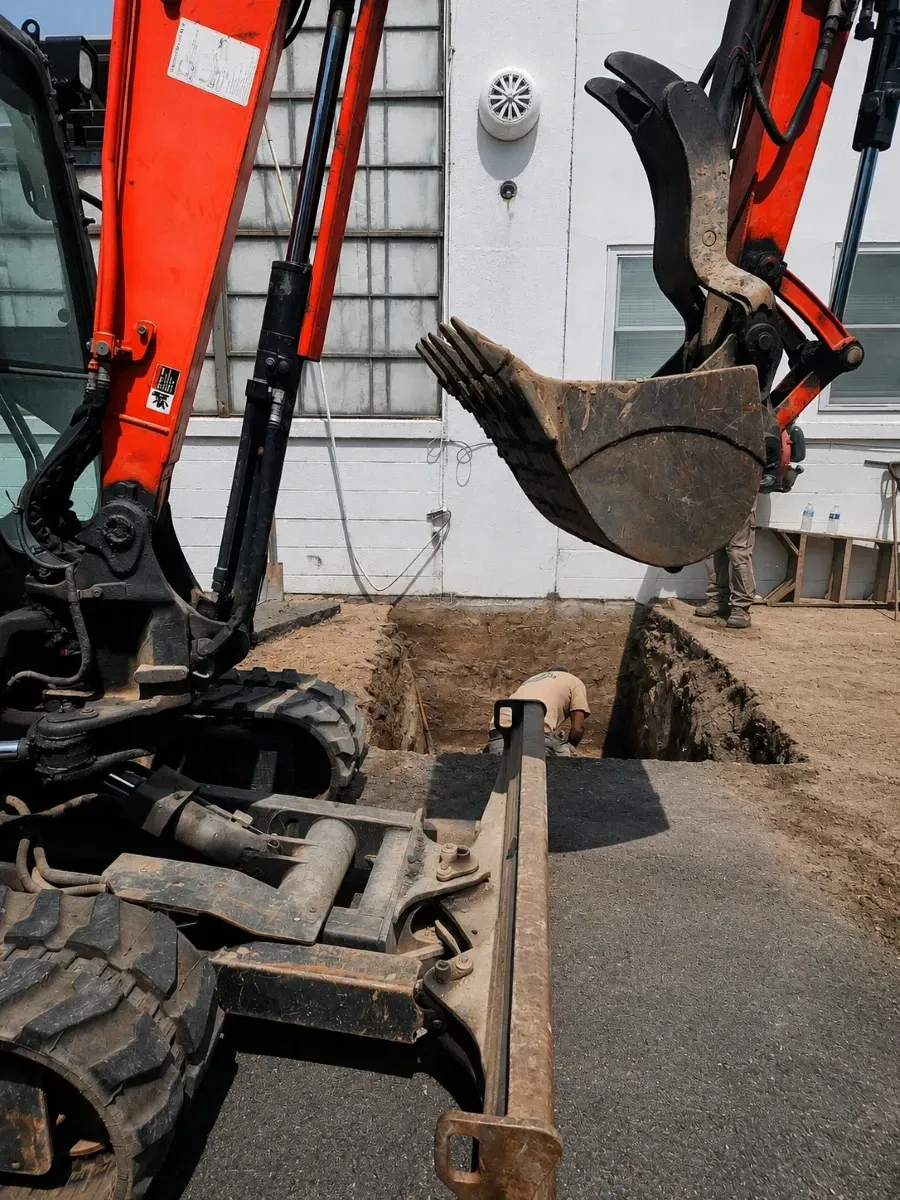 Excavator digging a trench at a construction site next to a building during underground utility work.
