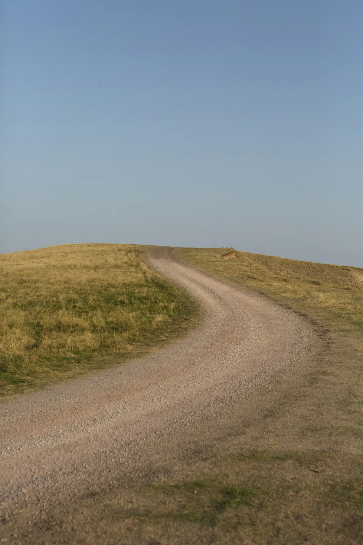 Gravel road curving through open grassy land.
