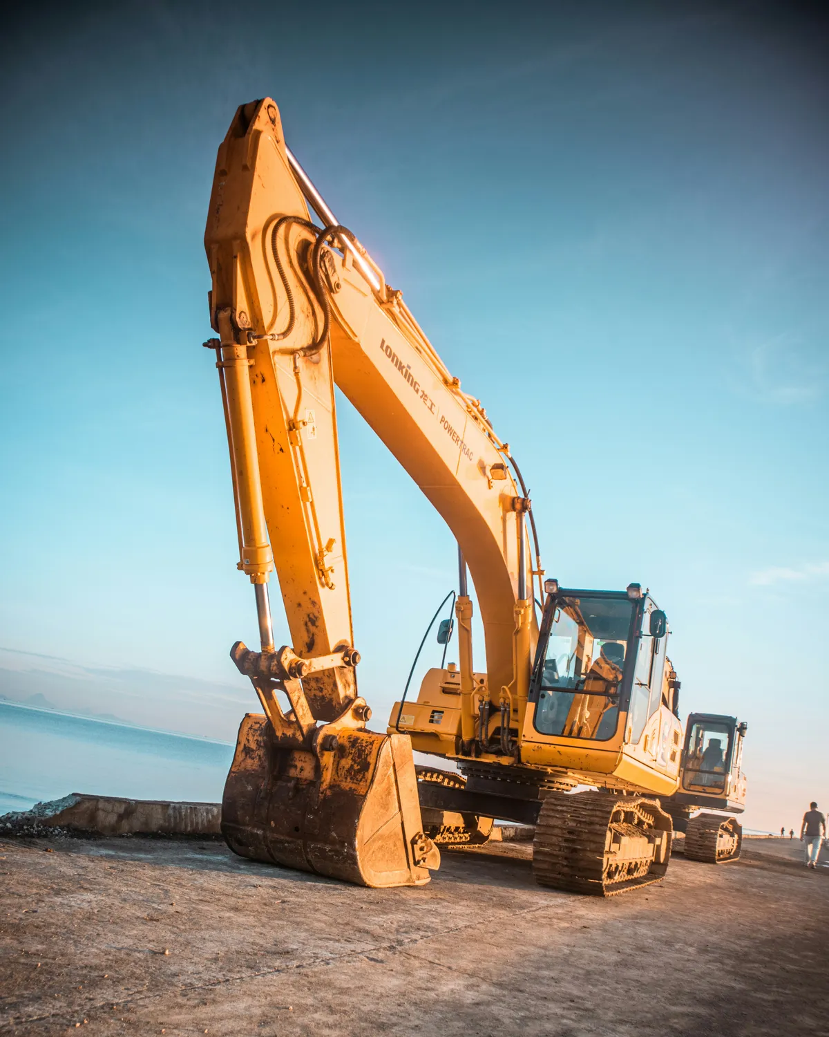 Orange excavator with its boom raised at an earthwork site.