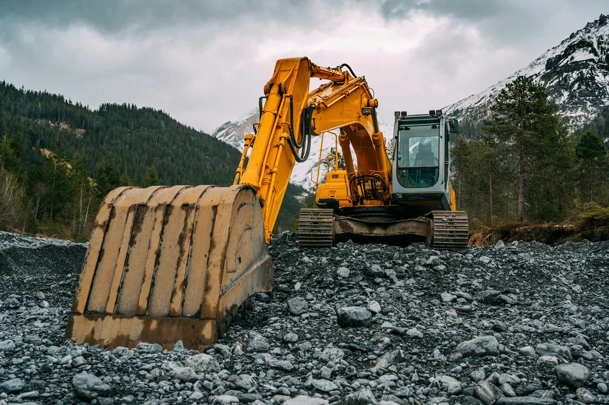 Excavator bucket and boom above exposed earth and stone.