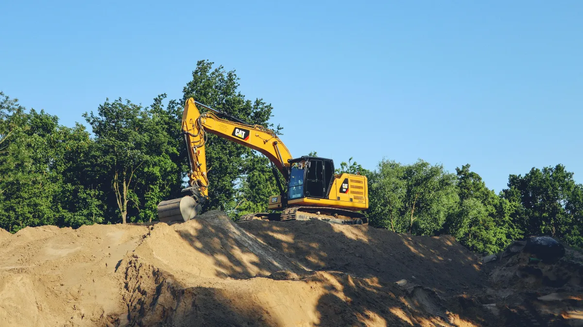 Excavator working on an exposed earthwork area beside trees.