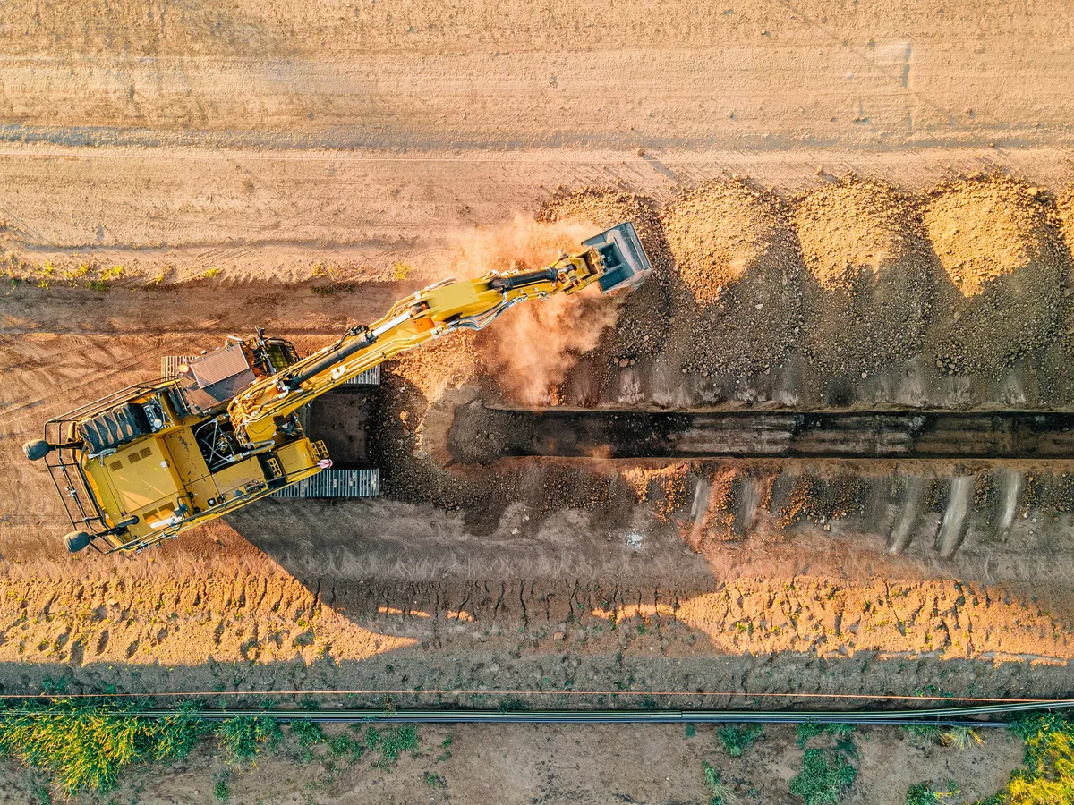 Tracked excavator working within a cut in exposed earth.